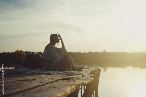 Attractive young girl in stylish clothing posing on a wooden Pier and Dreaming. Photo with Film and Grain Effect