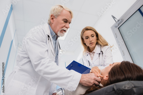 Selective focus of doctors with clipboard checking pulse of woman on stretch in clinic