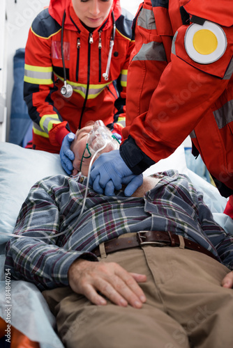 Selective focus of paramedics in latex gloves doing cardiopulmonary resuscitation to patient in oxygen mask