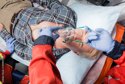 Selective focus of paramedic in latex gloves wearing oxygen mask on sick patient in ambulance car