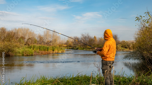 A fisherman in colorful clothes catches fish on a spinning rod in the river in autumn