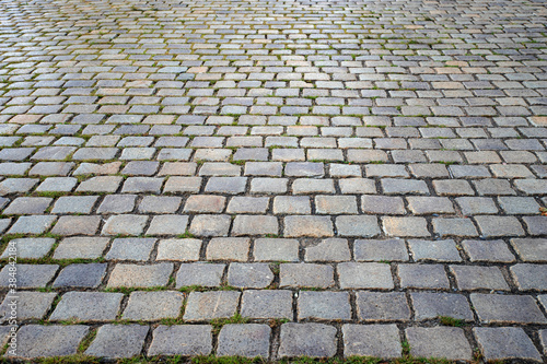 Neat paving stones with stones slightly wet from the rain. Wet pavement. Old cobblestone road, selective focus.