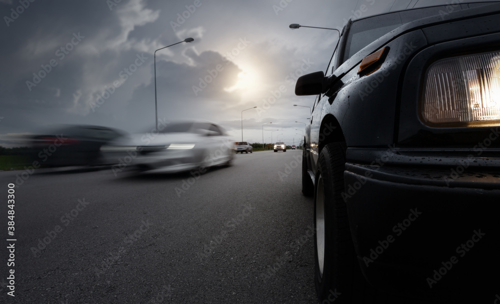 Black compact SUV car stop on wet road with speed blurry cars and storm clouds as background,.transportation during bad weather condition concept.