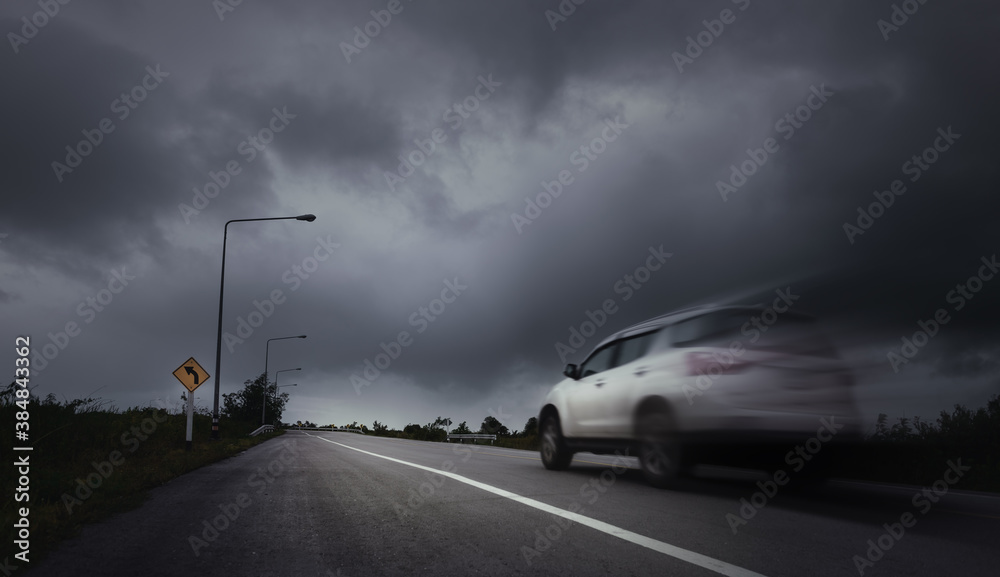 Blurry speed car running through sharp curve with arrow warning signs,dark stormy clouds over urban background.