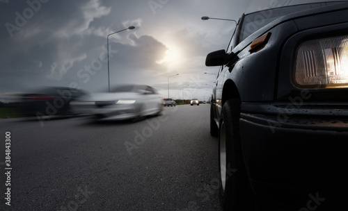 Black compact SUV car stop on wet road with speed blurry cars and storm clouds as background,.transportation during bad weather condition concept.