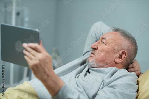 Grandpa using an electronic tablet while in bed.