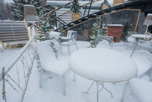 Tables and chairs in a cafe covered with snow outdoors.