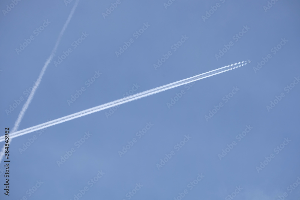 Long white planes traces crossing in the clear cloudless blue sky and big passenger supersonic airplane with four jet engines flying high Long white planes traces crossing in the clear cloudless blue sky and big passenger supersonic airplane with four jet engines flying high