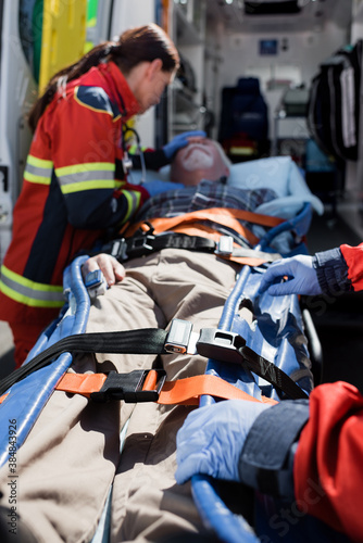 Selective focus of paramedics standing near patient on stretcher and ambulance auto