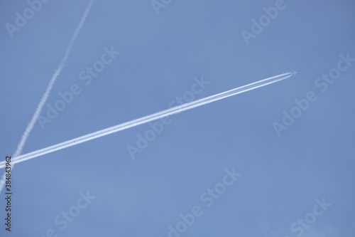 Long white planes traces crossing in the clear cloudless blue sky and big passenger supersonic airplane with four jet engines flying high