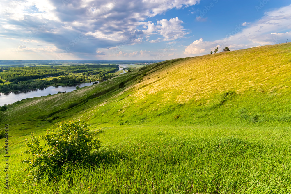 Sunny summer landscape with river,fields,green hills and beautiful clouds in blue sky.Pretty view of summer scenery on a nice day.Green trees growing along the river.