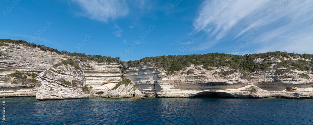 Panorama of vertical white rocks with vegetation against the sea and sky with clouds, copy space