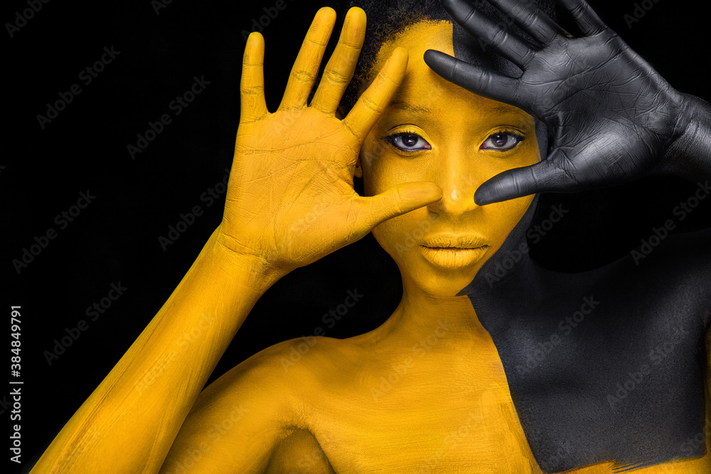 Face art. Woman with black and yellow body paint. Young african girl with colorful bodypaint. An amazing model with yellow makeup. Closeup face. - obrazy, fototapety, plakaty 