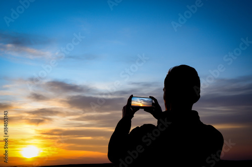 Silhouette of young man shoots sunset on phone  smartphone. Travel  walking.