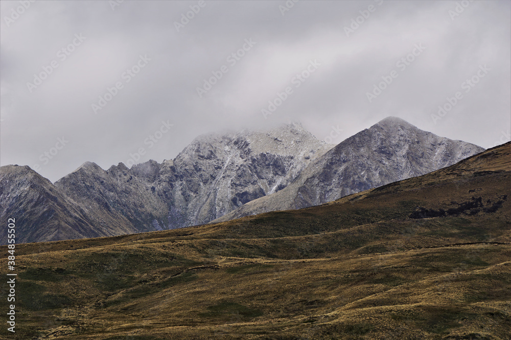 Mountains surrounded by clouds with lush grasses in the foreground along the Kepler Track near Te Anau in New Zealand