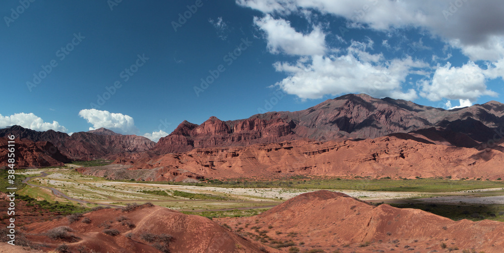 Desert landscape. Panorama view of the beautiful green valley surrounded by the red canyon, sandstone and rocky mountains under a blue sky with dramatic clouds.