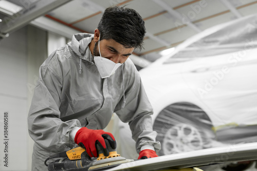 young caucasian professional car service male worker with orbital polisher, male polishing car body in auto repair shop