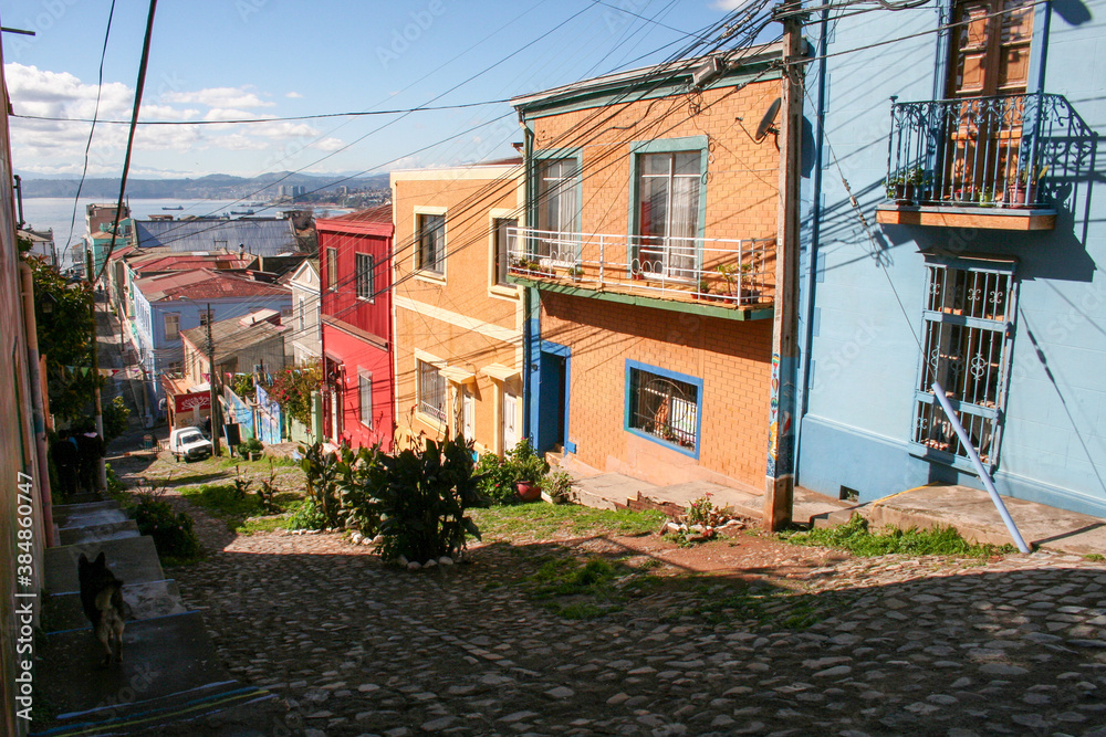 Pedestrian hilly street of Valparaiso with colorful houses and top view on city and ocean in sunny day