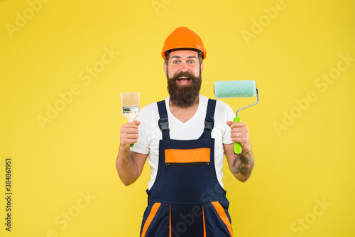 Moments of best creation. Happy decorator yellow background. Painter decorator hold paint roller and brush. Handyman or worker. Painting and decorating work. Design and decor. Renovation and repair photo