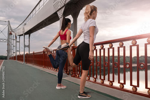 Full lenght photo of female friends doing stretching exercises outdoors