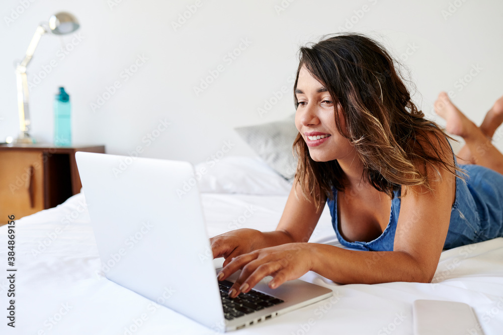 Smiling woman using a laptop on her bed Smiling woman using a laptop on her bed