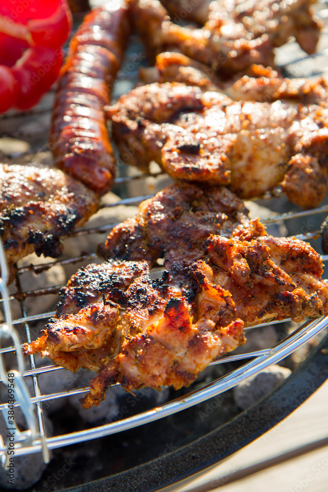 Chicken, sausages and red bell pepper being barbequed