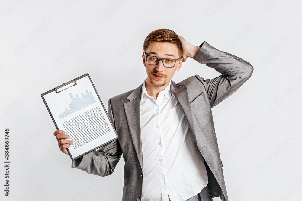 Young handsome brunet man in glasses in a suit is unhappy with business documents and charts on a white isolated background Young handsome brunet man in glasses in a suit is unhappy with business documents and charts on a white isolated background