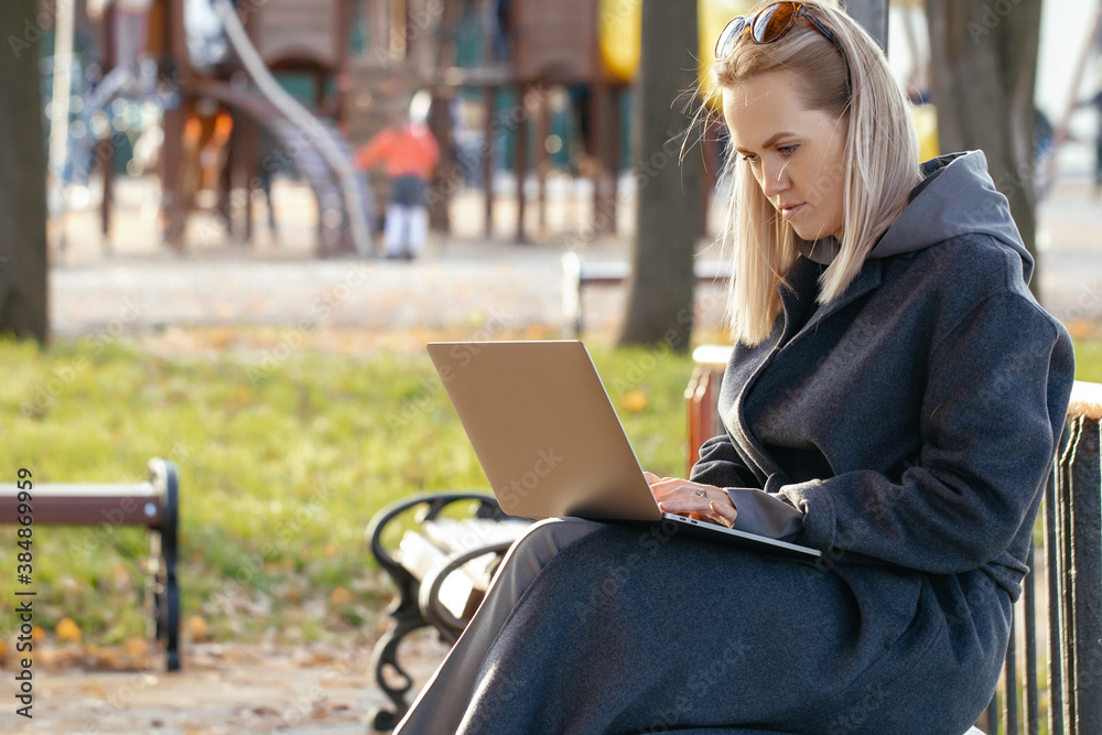 girl in a long gray coat with a laptop on her lap is sitting on a wooden bench in a Park, looking at the camera girl in a long gray coat with a laptop on her lap is sitting on a wooden bench in a Park, looking at the camera