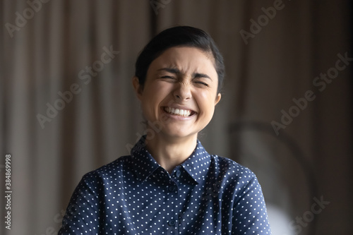 Close up of happy young indian woman laugh at funny joke at workplace. Overjoyed 20s millennial mixed race ethnicity female employee have fun smile feel optimistic in office. Happiness concept.