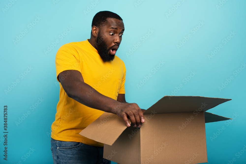 Happy boy receives a package from online shop order. happy and surprised expression. Blue background. - obrazy, fototapety, plakaty 