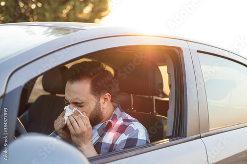 Young man sneezing while driving car. Healthcare, virus, allergy concept.