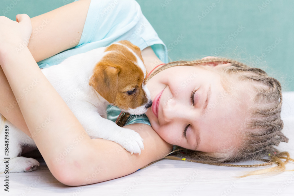 A beautiful girl of 8-9 years old lies on floor in an embrace with a little Jack Russell Terrier puppy. Love for dogs, taking care of pets. Childhood, friendship. Close-up portrait of a child and dog