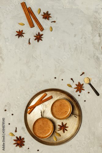 Hot fragrant masala tea in small copper cups on a round tray.On a grey stone background with spices, top view with space