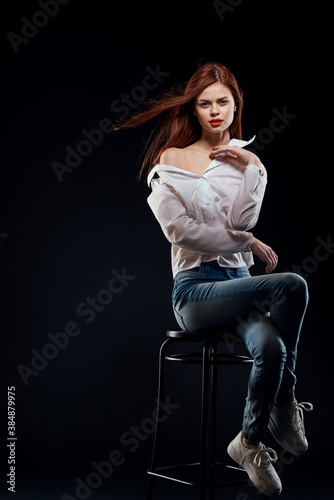 pretty woman sitting on a chair posing white shirt jeans long hair red lips dark background