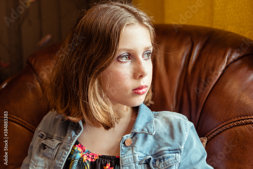 A natural portrait of a tween or teen girl with bobbed hair sat in an armchair, sad or melancholy thoughtfulness