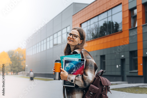 millennial caucasian female student in glasses and dental braces with books walking on campus after exam, lunch break. young smiling happy woman with backpack studying in college. University lifestyle