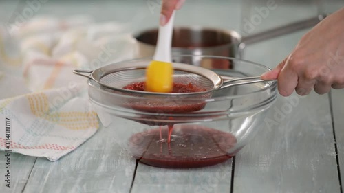 Woman strains berries through a sieve to make puree.