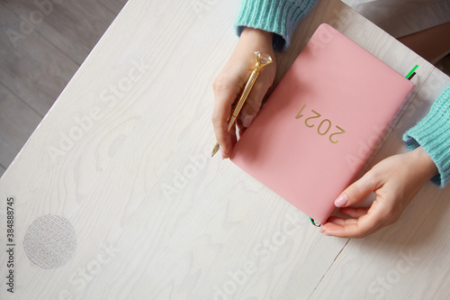 Woman sitting in knitted warm sweater with coral coloured 2021 diary on table