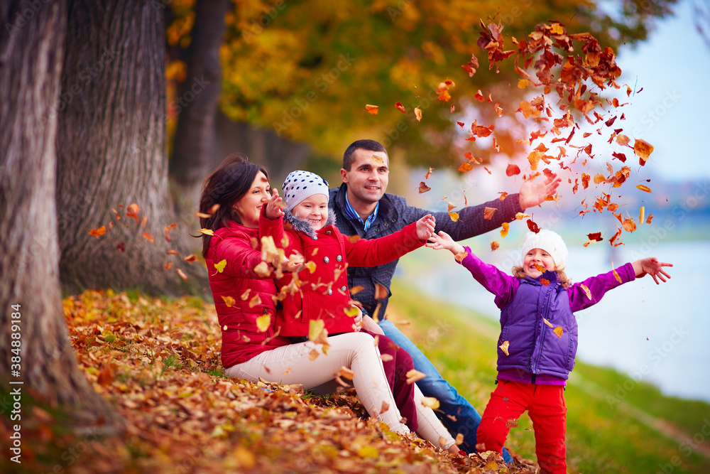 Fototapeta premium happy family playing among fallen leaves in autumn park