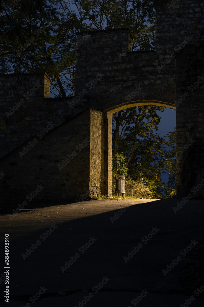 Obraz premium light from street lighting through the gate of the old wall from the 17th century in the center of Prague and a waste basket in a park in the Czech Republic at night