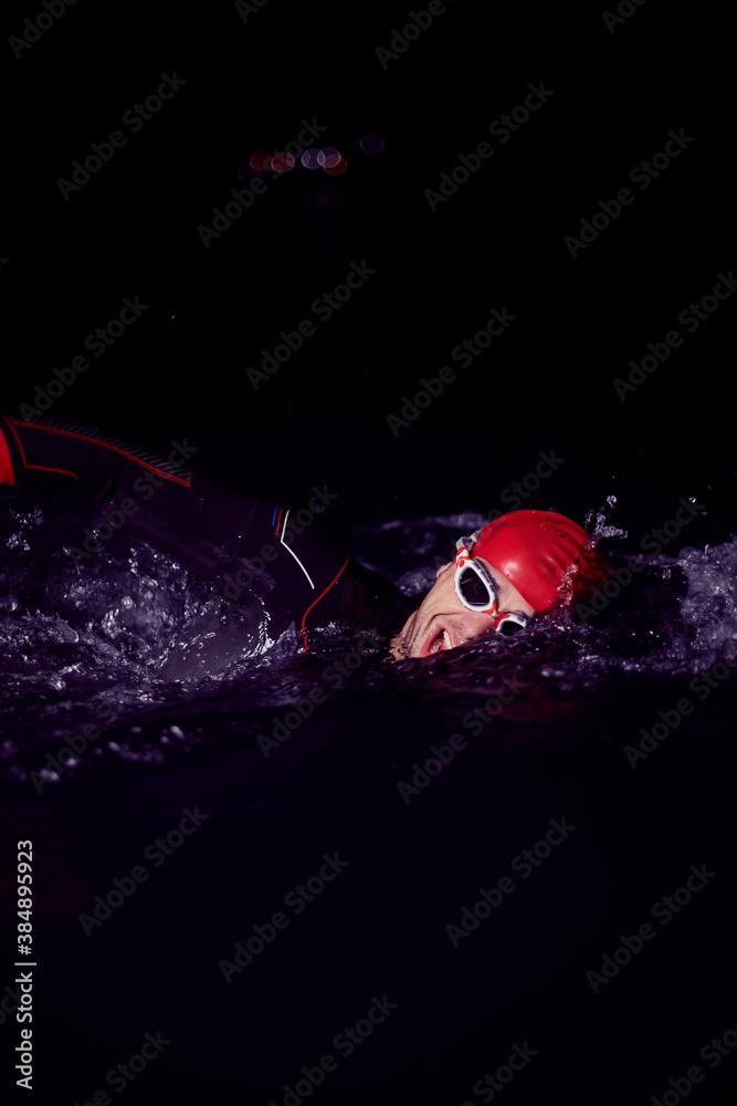 triathlon athlete swimming in dark night wearing wetsuit