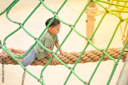 asia boy enjoying activity in a climbing adventure park on a summer day. Boy climbing ropes © wuttichok