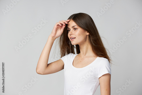 Beautiful woman holds her hands near her face and looks to the side in a white t-shirt 