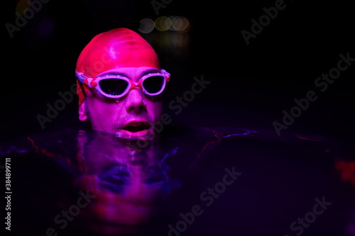 authentic triathlete swimmer having a break during hard training on night neon gel light