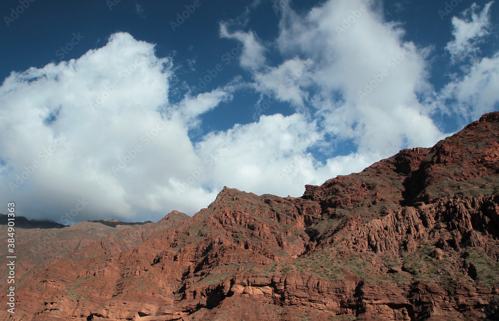 Brown and red mountain range. Geology. Panorama view of the rocky mountains and cliffs in the desert, under a dramatic blue sky with clouds. 