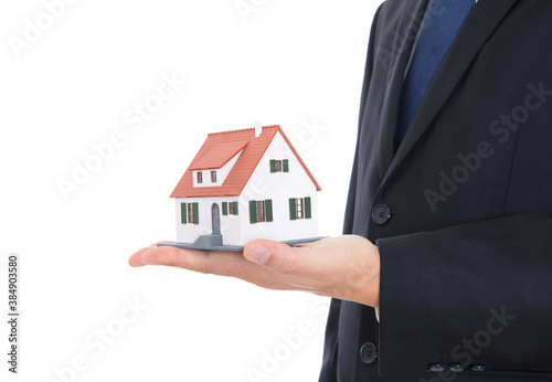 A house salesperson in a black suit and blue tie holds a small house model