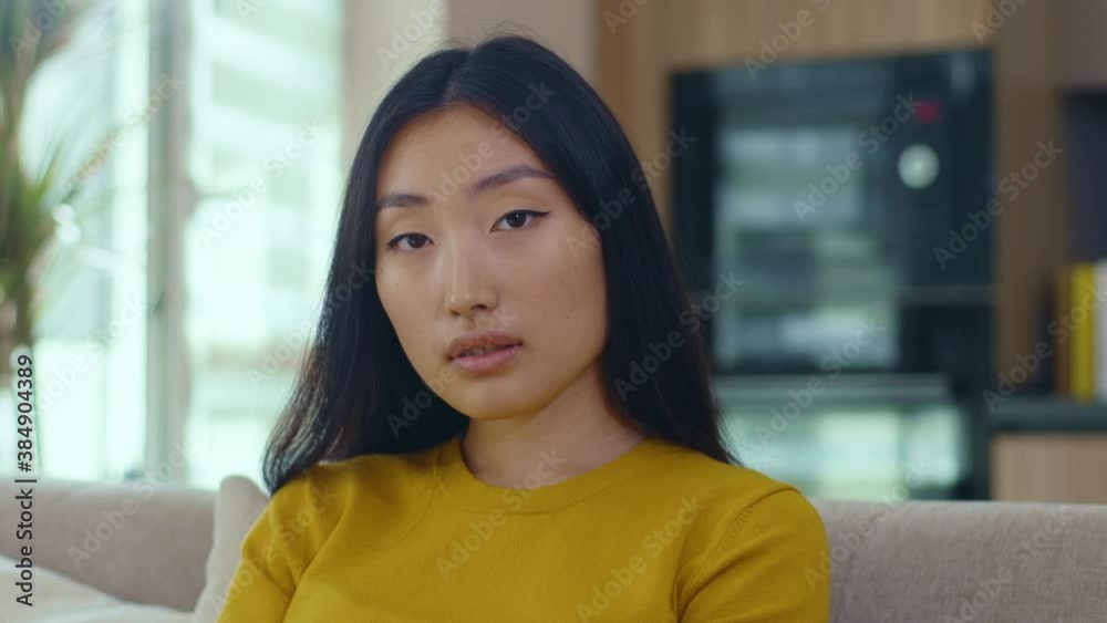 Attractive portrait asian young woman look at camera sitting on sofa at home. Feel confident successful. Sexy girl. Close up. Slow motion