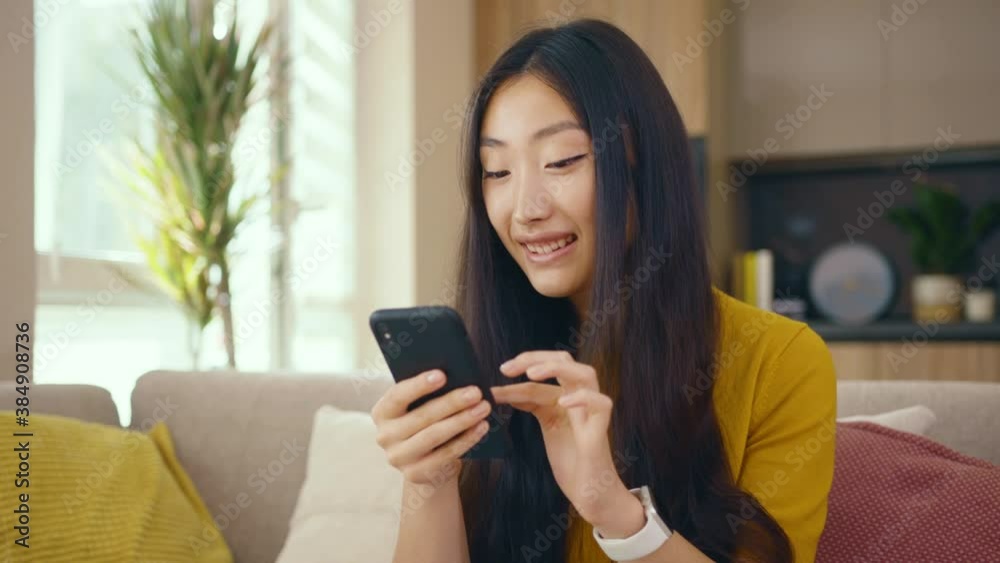Smiling asian young woman use phone sitting on sofa at home. Social media text email enjoy distant communication. Social media. Close up. Slow motion