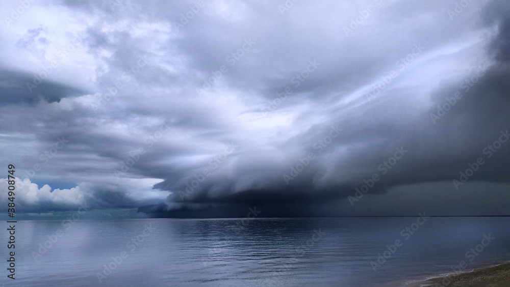 Obraz premium Dark storm clouds gather over Surigao Strait near Mabua Beach in the Philippines, showing calm coastal waters beneath an overcast sky and changing weather conditions along the shoreline.