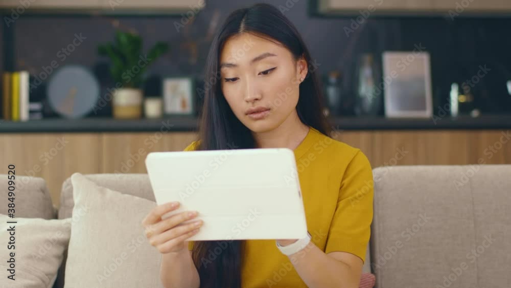 Portrait young asian woman sitting on couch in cozy room use tablet device look around at home. Businesswoman internet confident chatting. Portrait. Slow motion Portrait young asian woman sitting on couch in cozy room use tablet device look around at home. Businesswoman internet confident chatting. Portrait. Slow motion